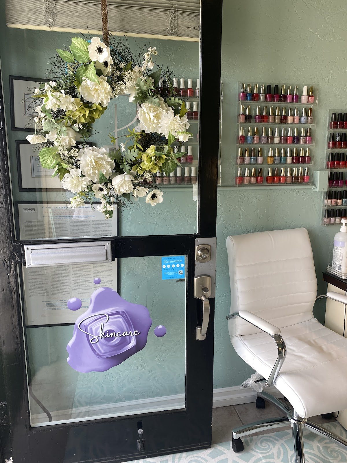 Front door with a white floral wreath and the wall of polish colors inside the studio